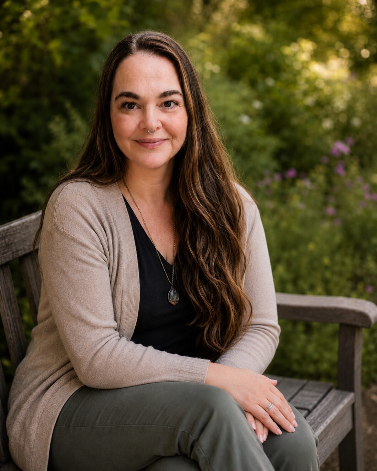 Nicole Sell, MSW, LSW, seated on a wooden garden bench in front of greenery and wildflowers, smiling at the camera.